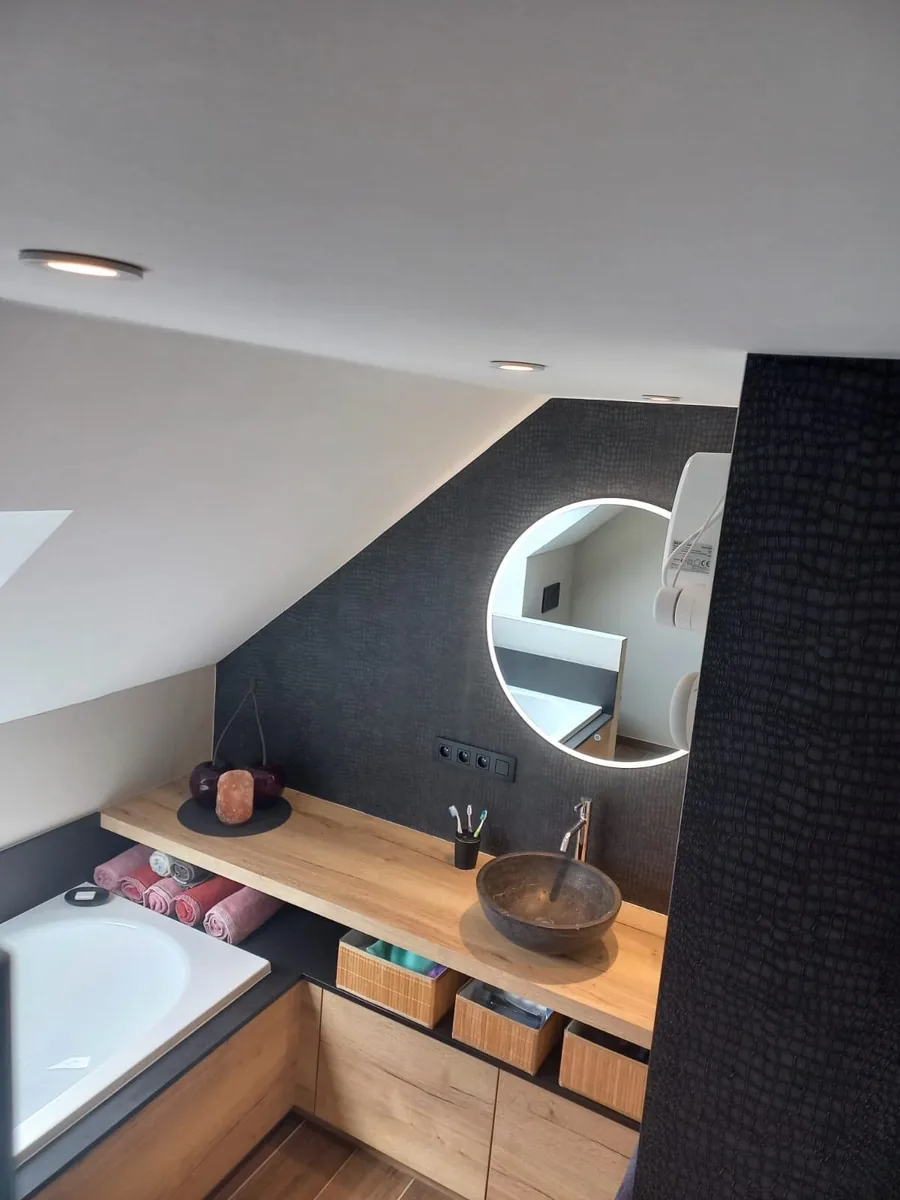 Dakbadkamer met donker mozaïek, ronde verlichte spiegel en stenen wastafel